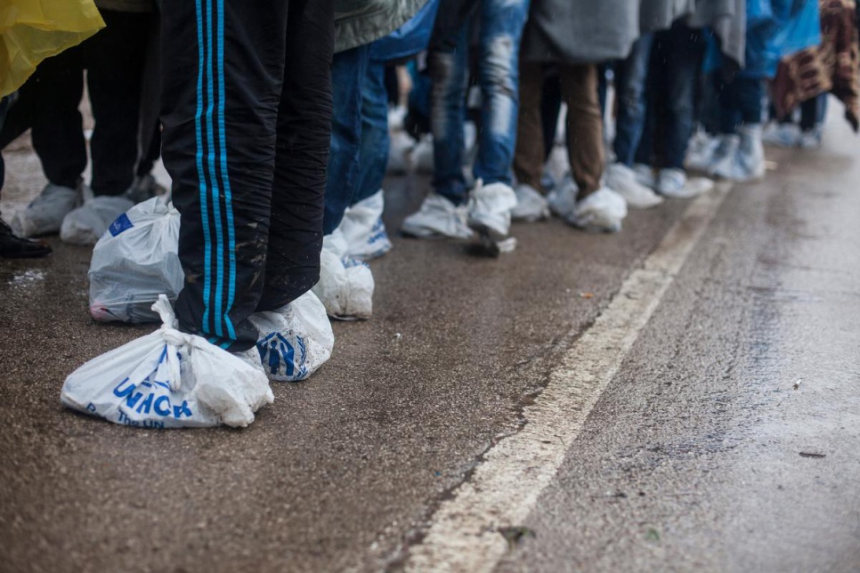 In the wet weather, refugees use plastic bags to keep their feet as dry as possible as they wait for a bus that will transport them to Opatovac transit centre.