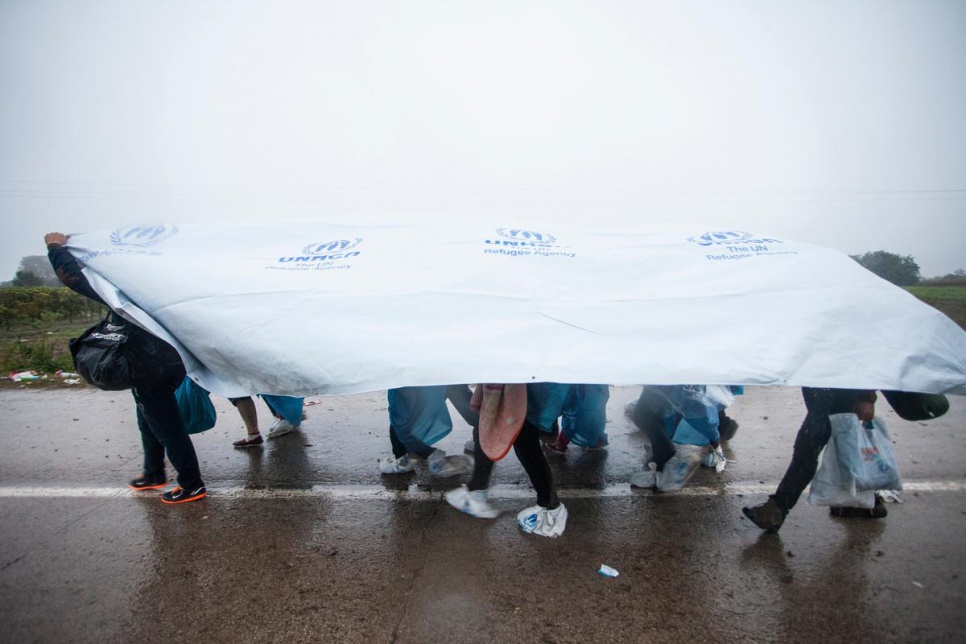 A group of refugees use UNHCR tents to protect themselves from rain in Bapska, Croatia.
