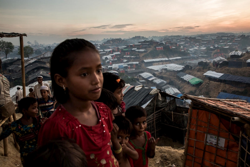 Young Rohingya refugees on a hillside at dusk overlooking a sprawling array of shelters.