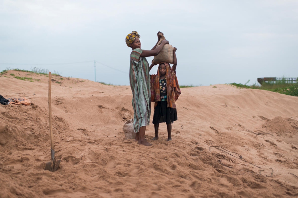 أم كونغولية وطفلتها نزحتا جراء الصراع وتعملان في مناوبة صباحية مبكرة لتعبئة ونقل الرمل من بحيرة تنغانيكا إلى مواقع بناء محلية. 