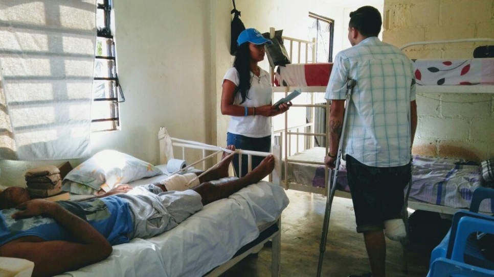 A man with an amputated leg stands with crutches and talks to an official. They are in a room with beds in it.