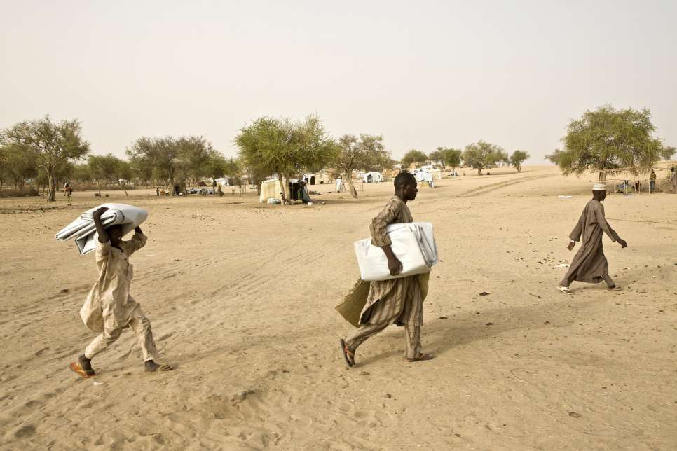 Bala, center, carries plastic sheeting to the spot allocated to his family to build their shelter at Sayam Forage camp in southern Niger. 