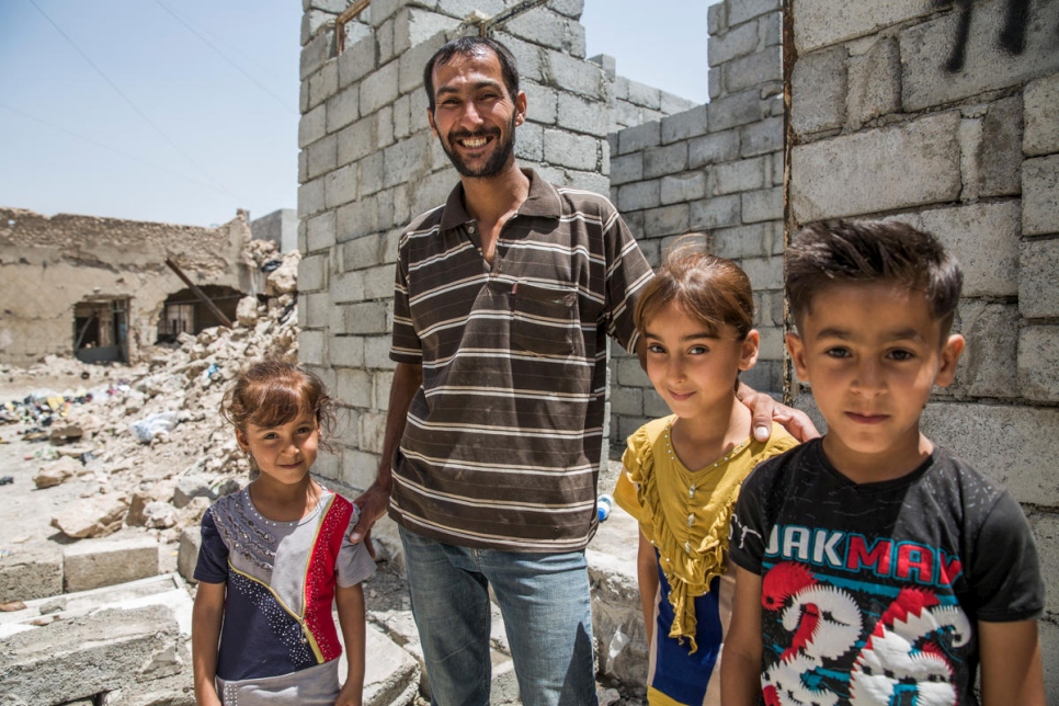 A displaced Iraqi father stands with his three children outside the new home he is building in West Mosul, Iraq.