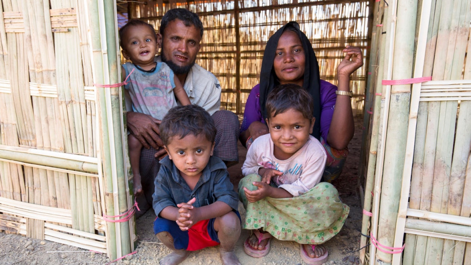 Mohammad Harez and Momena Begum squat at the entrance of their new shelter with children Mohammad Anas, 7 months, Mohammad Shohaib, 3, and Sohana, 6.