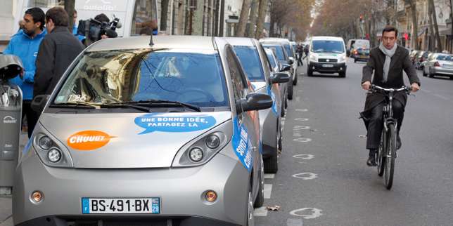 A man rides his bicyle past Autolib electric bluecars parked on December 2, 2011 in Paris, on the day of the official presentation of this public system of self-service, point-to-point electric rental cars, starting on December 5, 2011. 250 cars are already available in Paris and a ring of 46 surrounding communities and 2,000 should be available at the end of June 2012. This service, inspired of the successful Velib (bicycles self-service) is a first world event, at this scale. AFP PHOTO PATRICK KOVARIK / AFP PHOTO / PATRICK KOVARIK