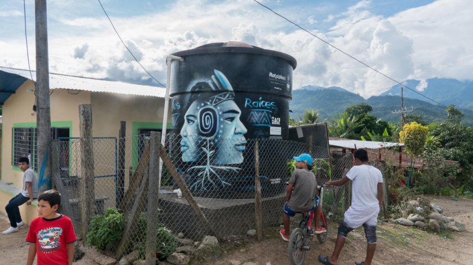 Children stand next to a water tank at the entrance to Nueva Esperanza. The tank, which provides clean water to the community, was installed with the aid of UNHCR in 2016.