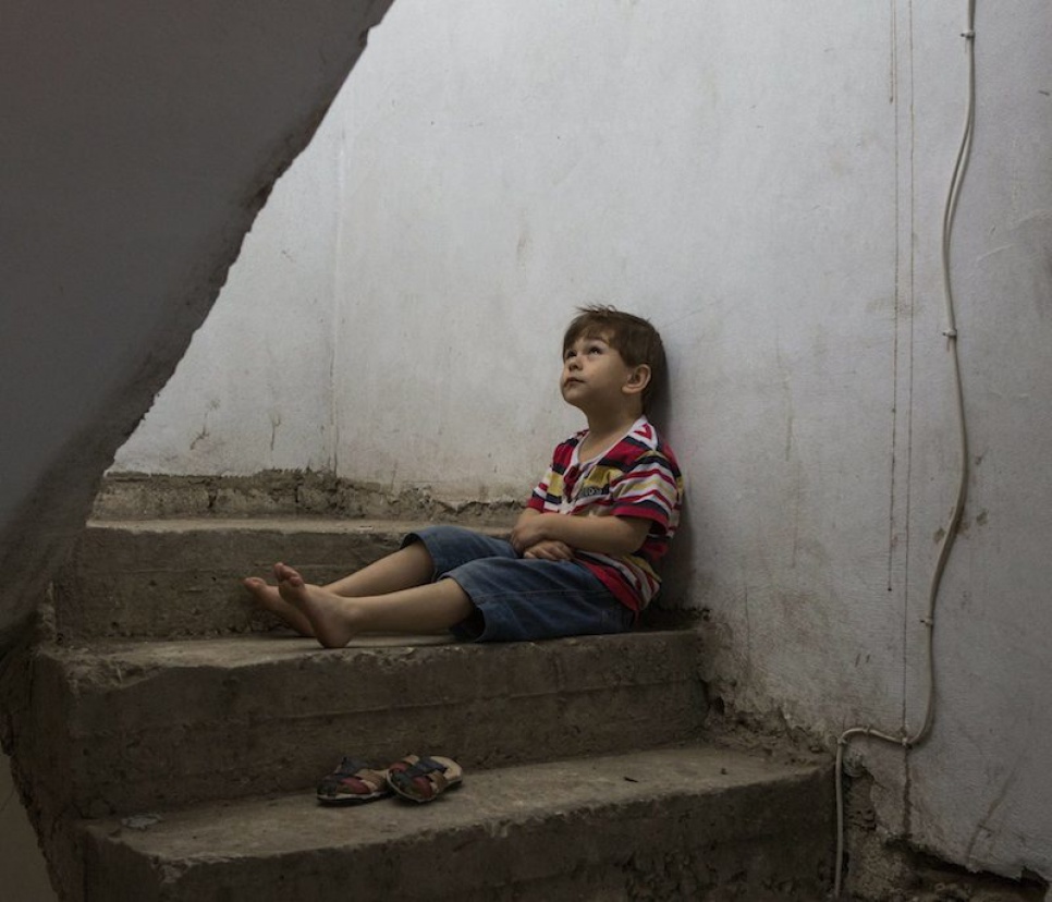 Omar, 8, sits in the stairwell of the building where he and his family have been living as refugees in Lebanon.