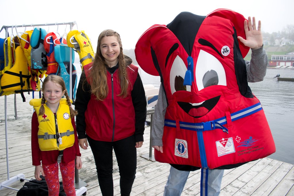 Young girl wearing a lifejacket, Red Cross staff and mascot Buckles.