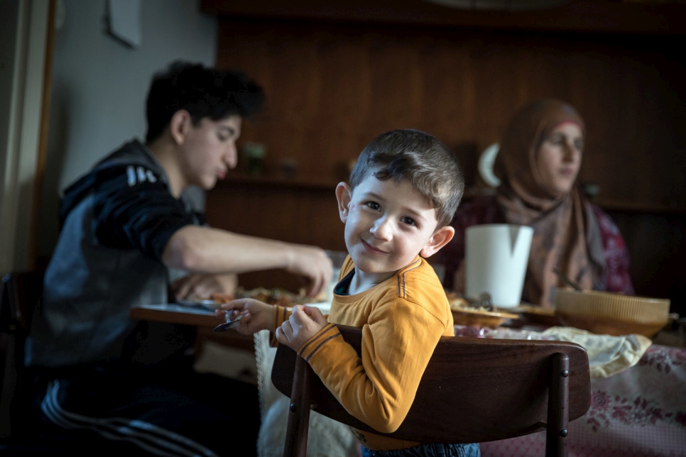 A younger member of the extended family, now reunited in Austria, enjoys a meal with his mother and cousin.