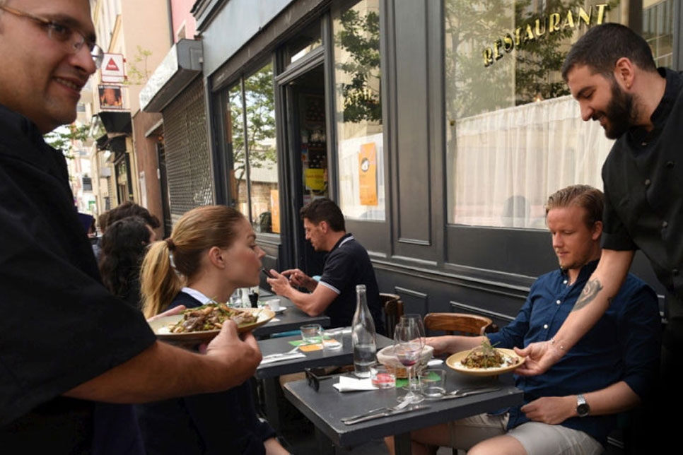 يقدم الطاهي السوري اللاجئ نبيل عطار (إلى أقصى اليسار) الأطباق مع صاحب المطعم وليد ساهد (إلى أقصى اليمين) في مطعم "لي بانتان" في باريس.