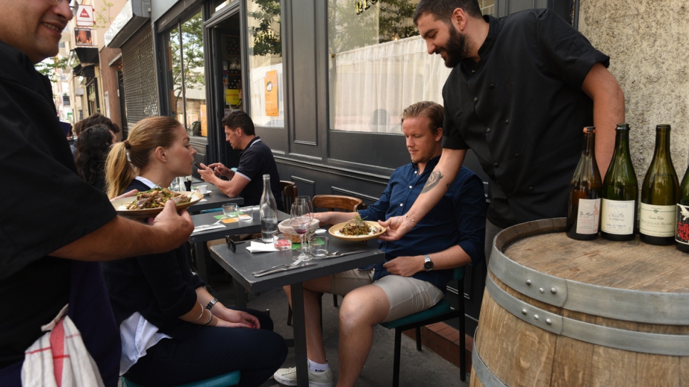 Le chef réfugié syrien Nabil Attar (tout à gauche) sert des plats avec le restaurateur Walid Sahed (tout à droite) au restaurant Les Pantins à Paris. 