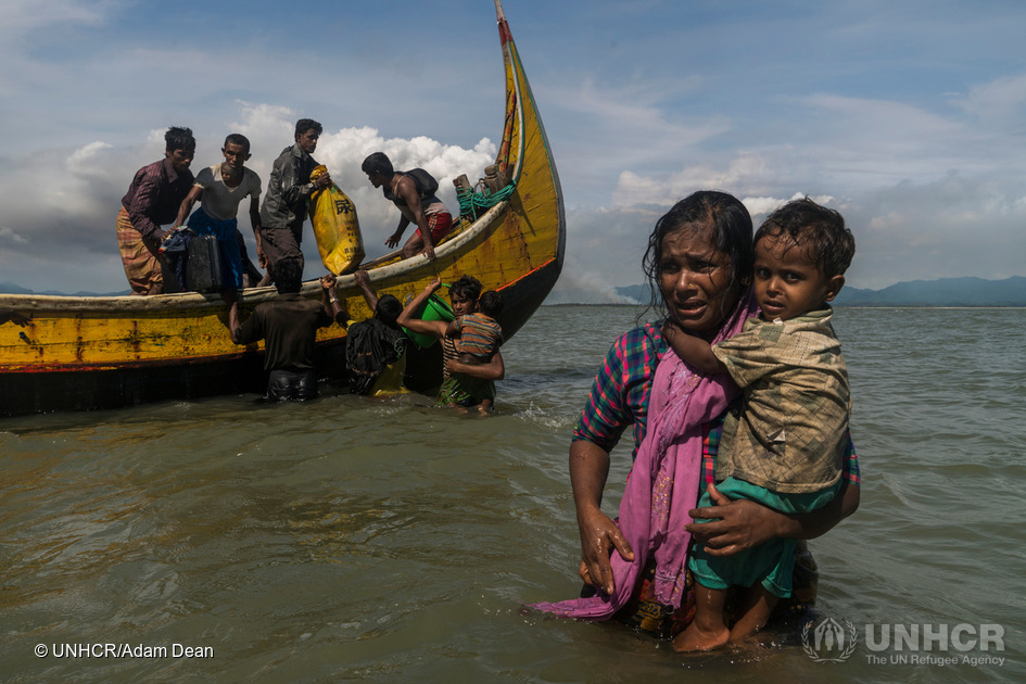En mor med sitt barn i famnen vadar mot stranden i Dakhinpara i Bangladesh. © UNHCR / Adam Dean