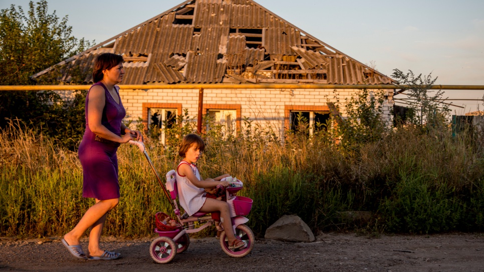 A mother and daughter stroll past a house partially destroyed in the 2014 conflict in eastern Ukraine.
