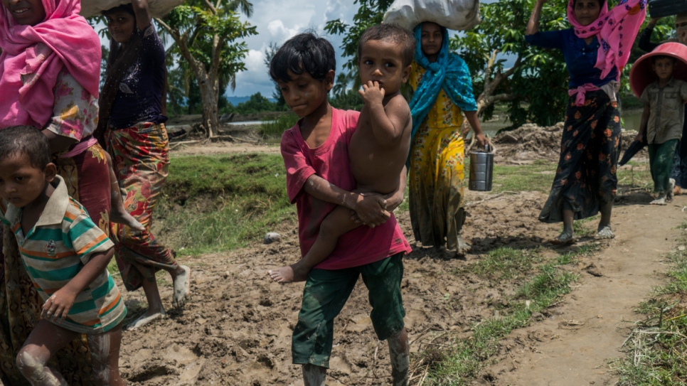 A Rohingya boy carries his little brother as he crosses with his family into Whaikhyang, Bangladesh.