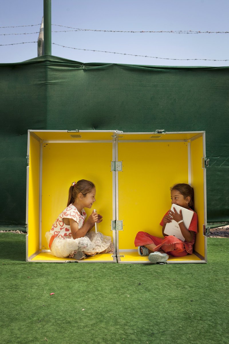 Two smiling girls sit in a yellow box on a green background.