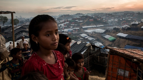 Young Rohingya refugees on a hillside at dusk overlooking a sprawling array of shelters.