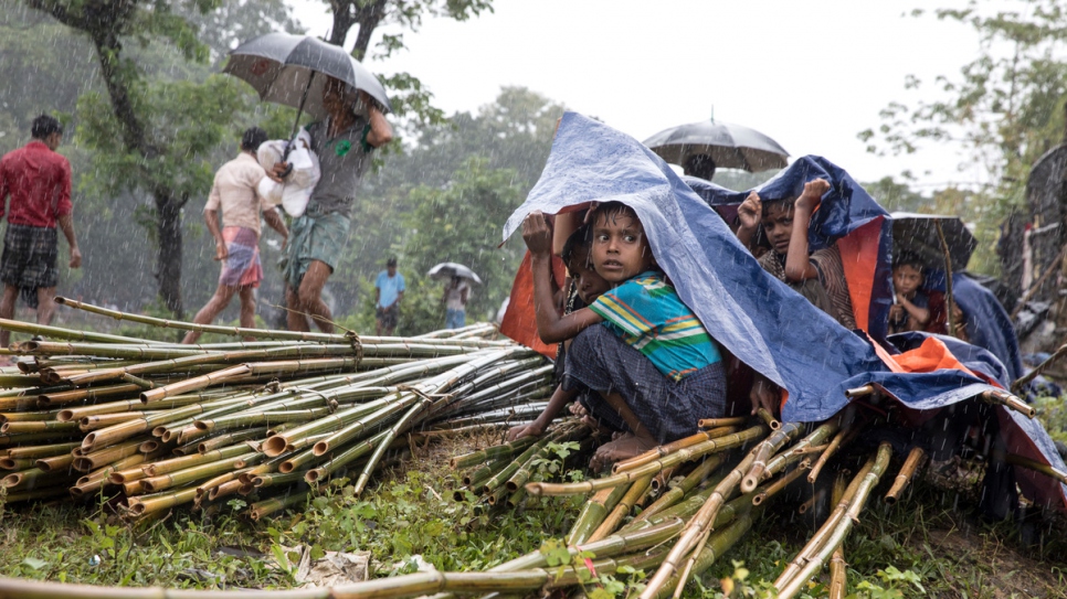 Rohingya children shelter under tarpaulin as heavy rain falls at Kutupalong.
