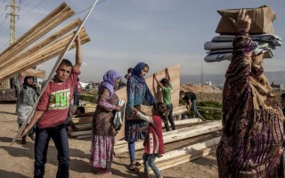 Syrian refugees at an informal settlement in Lebanon carry aid items, including wood to strengthen their shelters for winter.