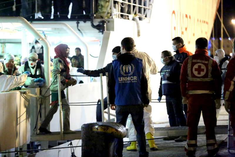 A UNHCR staff member watches as people rescued from the Mediterranean disembark from an Italian Coastguard vessel at Palermo, Sicily, this morning.