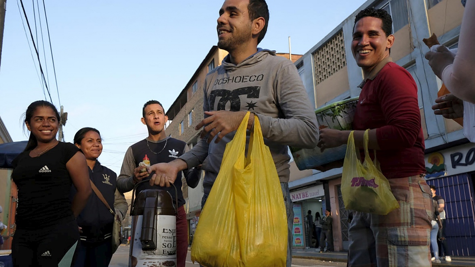 Luis Antonio Pérez (centre), 24, from Barquisimeto, Venezuela, sells hot chocolate and sweet bread outside the Migrations headquarters in Lima, Peru, accompanied by fellow street vendors from Venezuela.
