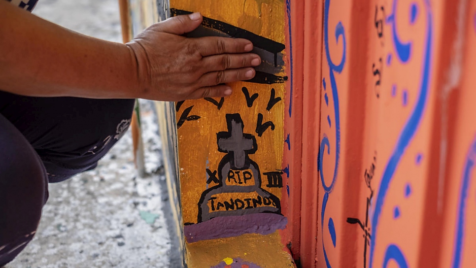 Janeth shows the tomb she painted in the mural to express her grief. Her 17-year-old son was killed by a criminal gang in El Salvador in 2017 because he refused to join.
