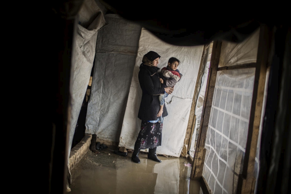 جورية رمضان تحمل أحد أبنائها وهي تتفقد مأواها الذي غمرته مياه الفيضان في مخيم الدلهمية العشوائي في سهل البقاع، لبنان.