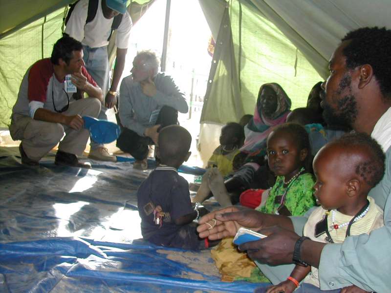 Un miembro del equipo de emergencia de ACNUR informa a Julien Clerc, Embajador de Buena Voluntad de ACNUR, sobre la atención que se proporciona a los refugiados en el centro de tránsito de Touloum, el 3 de marzo de 2004.