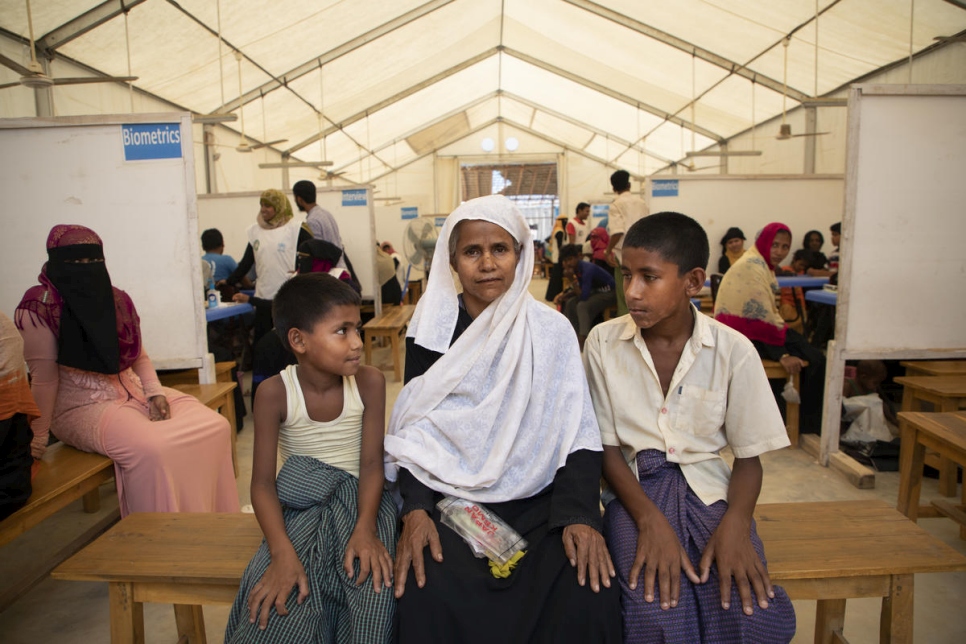 Nisa Alin, de 52 años, sentada con su hijo y su nieto (izquierda) en un centro de registro en el campamento de refugiados de Kutupalong (Bangladesh). "Estos documentos nos ayudarán a regresar", nos cuenta Alin, que huyó de la violencia en Myanmar en 2018.