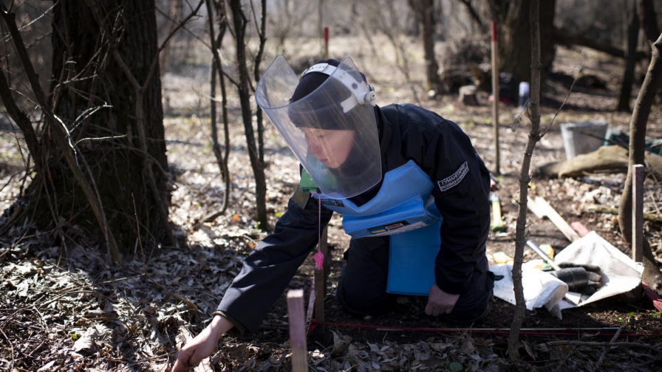 Deminer Tetiana Nikiforova, 37, searches through dried leaves for landmines.