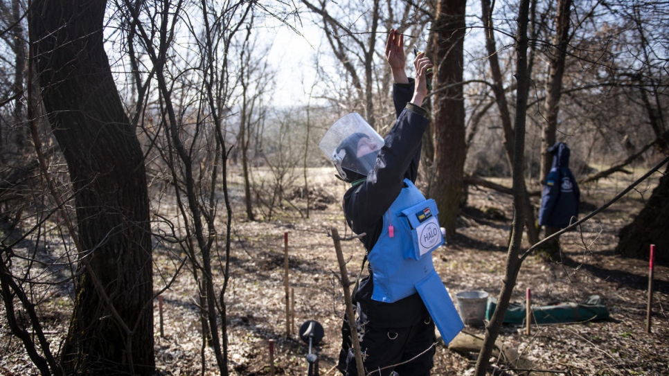 Tetiana coupe des branches d'un arbre tandis qu'elle recherche de mines terrestres et des mines à fil-pièges. 