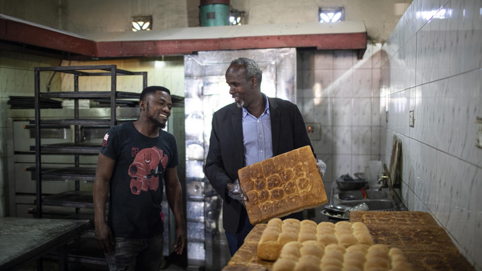 Hassan Abdi, réfugié somalien et propriétaire d'un restaurant (à droite), en conversation avec un employé zambien dans son restaurant situé dans la banlieue de Lusaka, Zambie. 