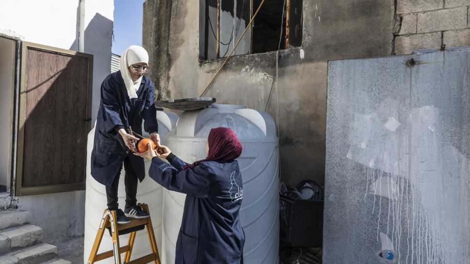 Buthayna, une réfugiée syrienne en formation, aide Safaa à poser une cuve à eau à Irbid, Jordanie. 