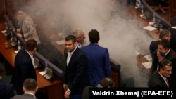 Kosovo lawmakers stand amid tear gas after canisters were released by opposition lawmakers during a parliament session in Pristina on March 21.