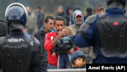 A migrant man holds a child standing in front of a Bosnian police cordon at the border crossing in Maljevac on October 26.