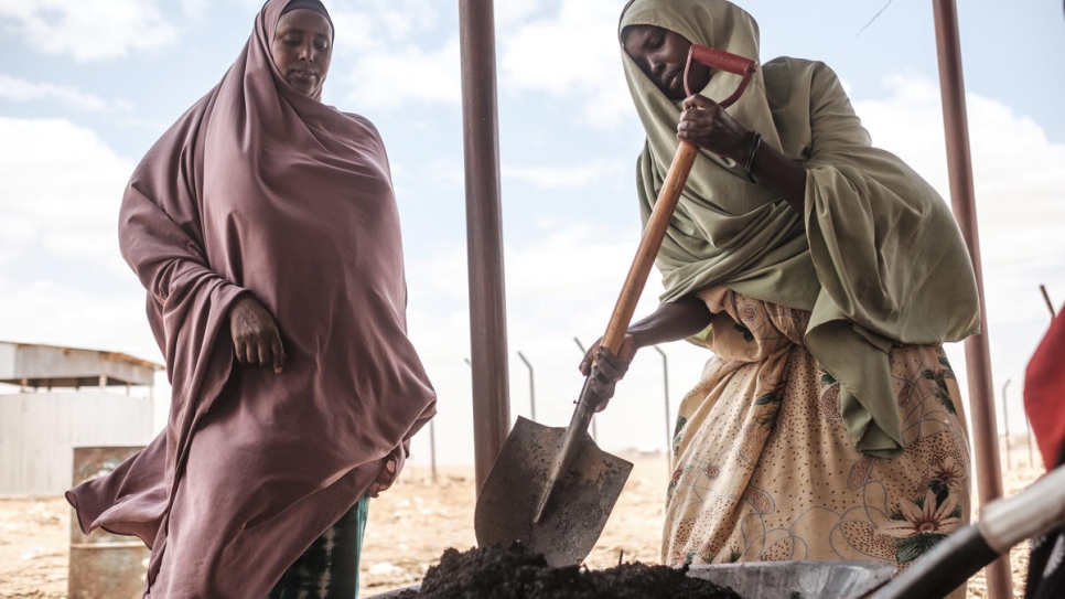 Somali refugee Saredo Abdi, 26, (right) turns by-products of Prosopis Juliflora with a shovel at a processing center in Bur Amino, Ethiopia.