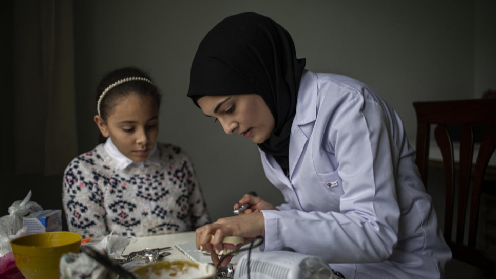 Sidra practices her dentistry skills at home while her younger sister Isra looks on.