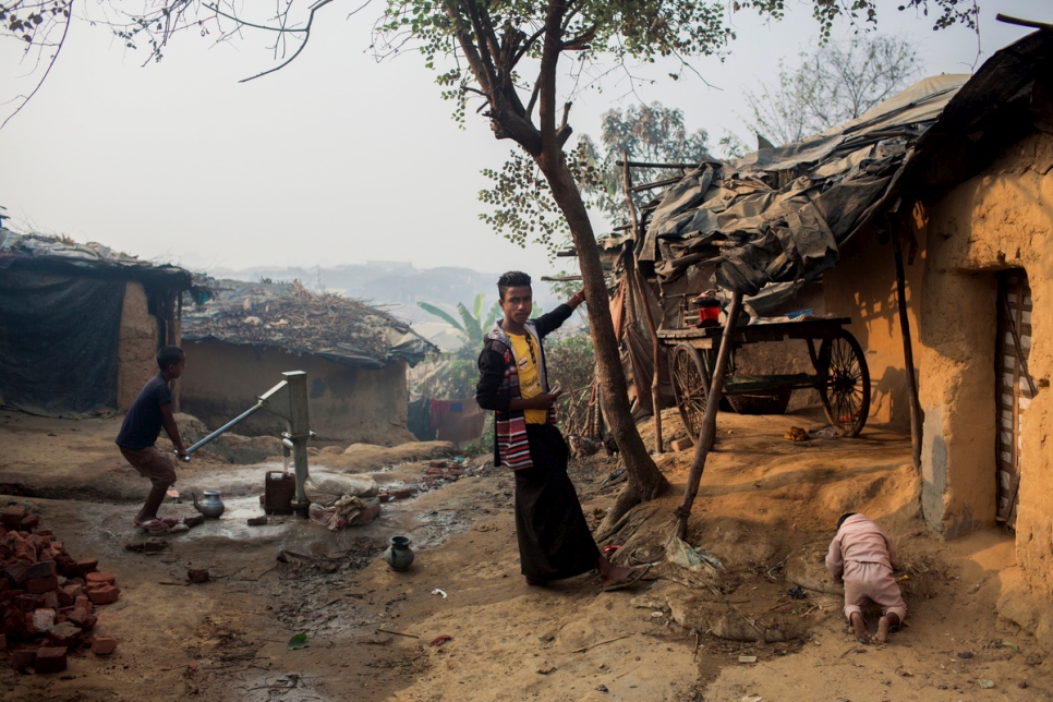 A boy from a recently arrived Rohingya family pumps water from a well at a makeshift site in Cox's Bazar, Bangladesh while his brother watches the baby outside their shelter. Thousands of Rohingya are living in the area since fleeing the October 2016 violence in Myanmar.