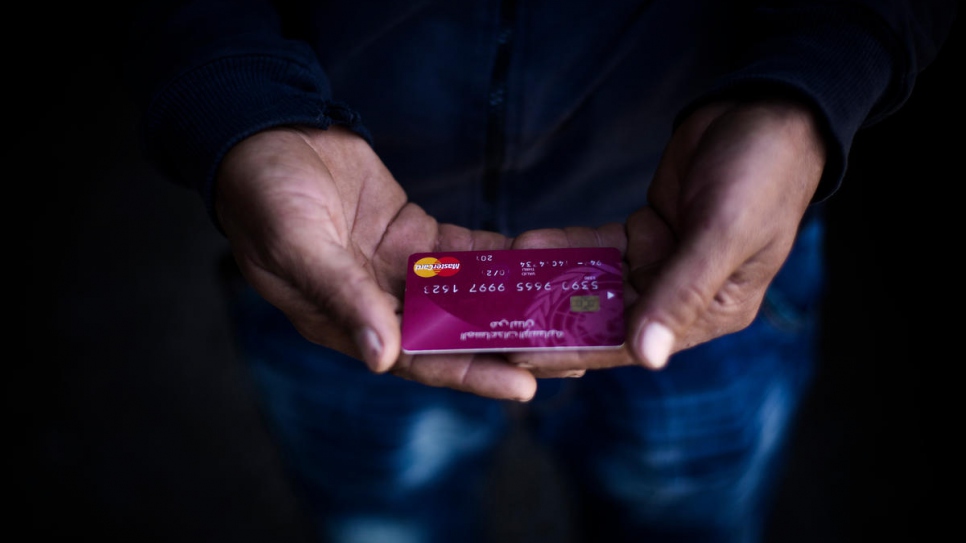 A young Syrian refugee holds an ATM card provided by UNHCR inside a distribution point in Tripoli, Lebanon, April 2018. She will use the cash to provide for her daughters, aged four and six.