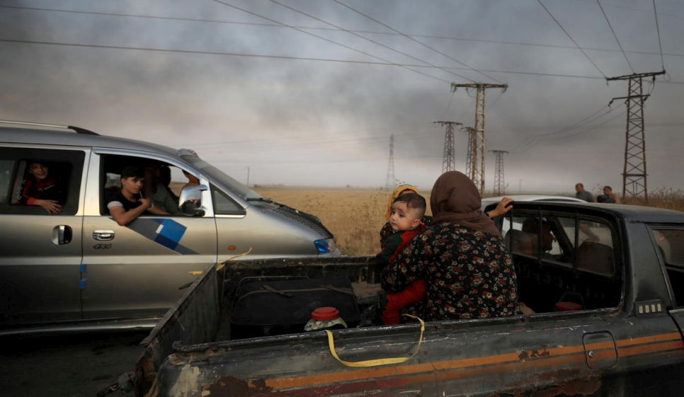 Syria. A woman with a baby sits at a back of a truck as they flee Ras al Ain town