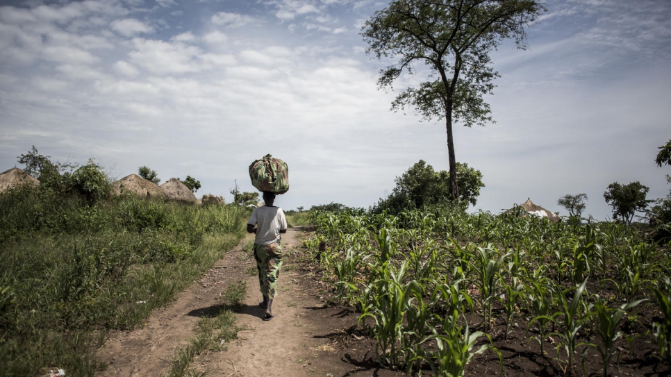 Neema porte un sac d'aubergines récoltées sur des terres qu'elle cultive avec des réfugiés et des agriculteurs locaux. 