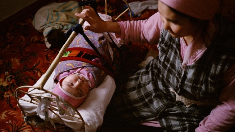 Une femme berce son bébé de huit mois dans son berceau, à Tastubek, Kazakhstan