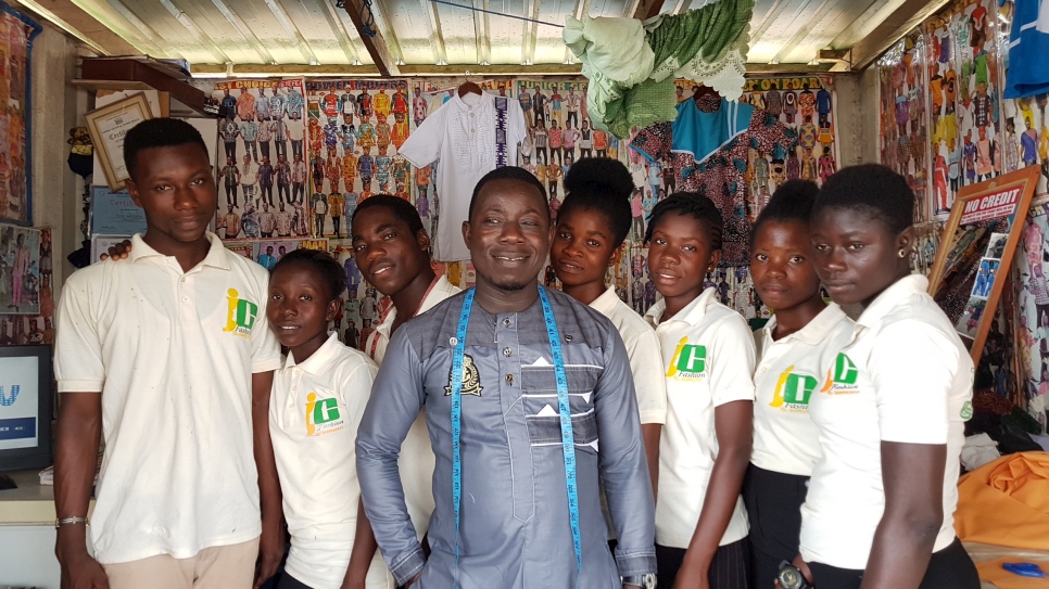 Ivorian refugee Bouhe Jean Claude poses with his staff in his tailoring shop in central Ghana.