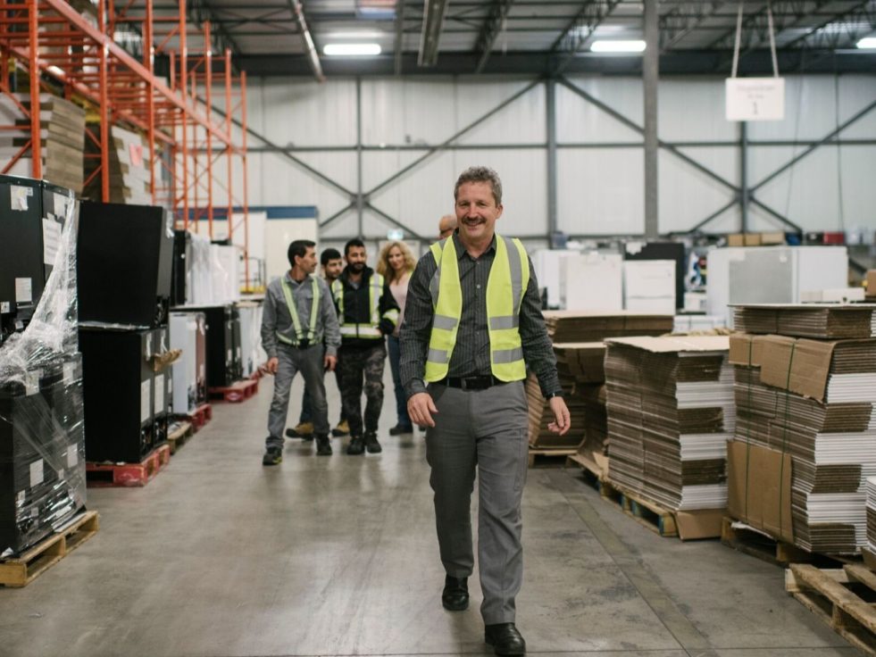 A man walks through a warehouse as his employees look on