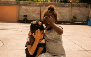 Two refugee children in Mexico pose for the camera with their hand covering their face