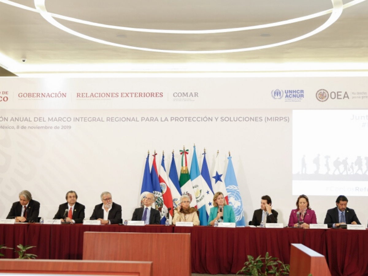 A group of people sit at a table with flags behind them