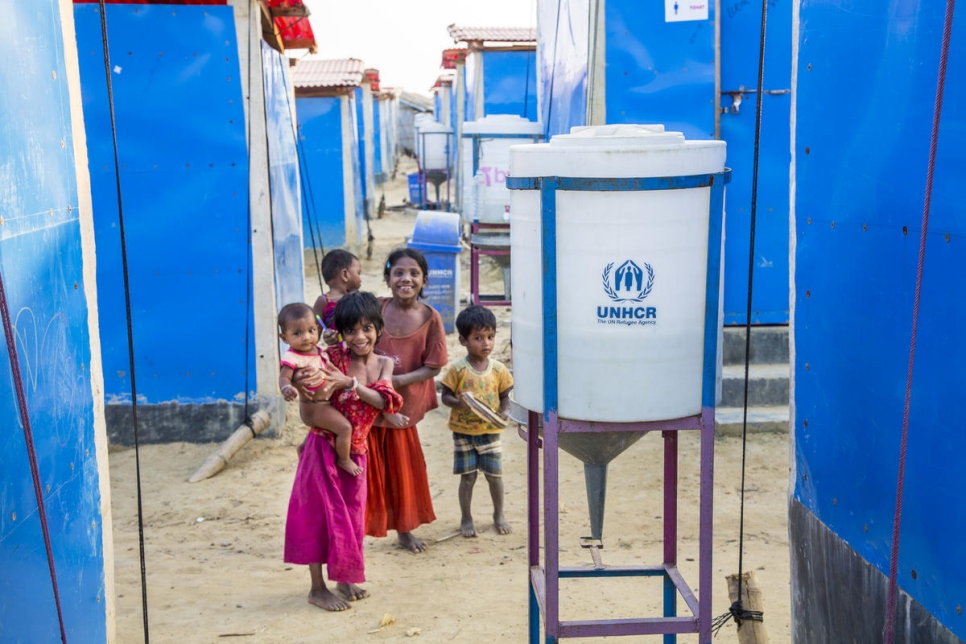 Rohingya children playing among blue tents and safe water cylinders