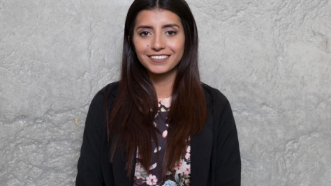 Portrait of a young woman standing against a grey background.