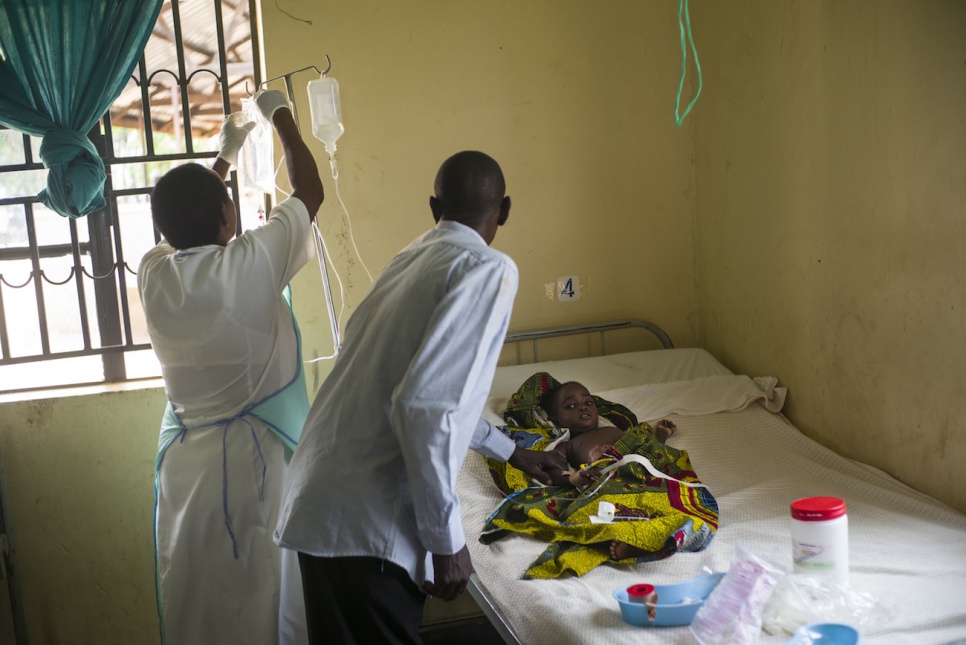 John comforts his daughter, Agness, who has been diagnosed with malaria, as a health worker makes her rounds.