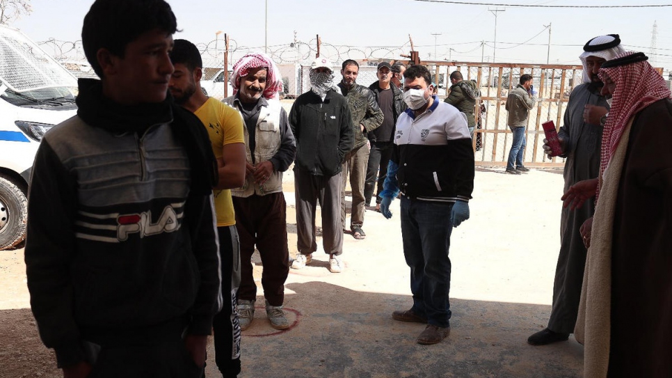 Refugiados en fila para el pan esperan en marcas dibujadas en el suelo para mantener el distanciamiento social.