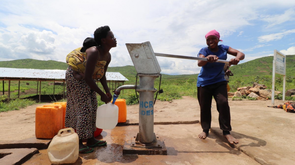 Aisha (right) pumps water from a borehole in Mulongwe settlement, Democratic Republic of the Congo.
